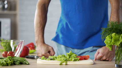 Young man getting ready to make fresh green salad in kitchen, husband cooking