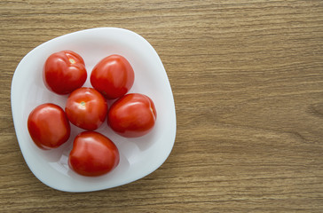 View of fresh tomatoes on a white plate on a wooden table.