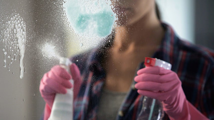 Experienced housewife spraying lot of washing-up liquid on window to clean it