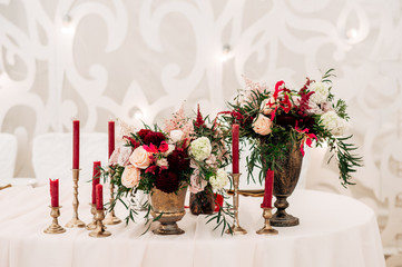 Decorate table with white tablecloth, red bouquets with fern and eucalyptus in brass vases