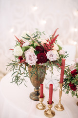 Decorate table with white tablecloth, red bouquets with fern and eucalyptus in brass vases