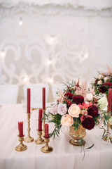 Decorate table with white tablecloth, red bouquets with fern and eucalyptus in brass vases