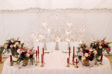 Wedding table decorated with candles and flowers in burgundy color in brass vases
