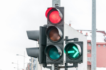 Close up of traffic light on the crossroad with red light for straight direction but green arrow for right turn only in the cold winter day with cloudy sky, traffic light