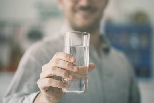 Happy young man holding glass of water inside