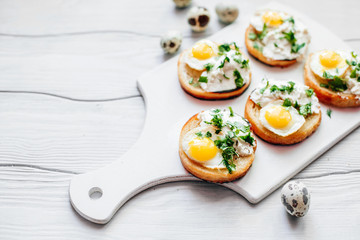  Sandwiches with ricotta and quail eggs with greens on a white board on the table