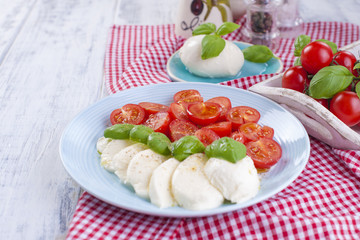 Traditional Italian salad with fresh cherry tomatoes and soft mazarella cheese, with basil and olive oil. Ingredients for salad. Portions in plates.