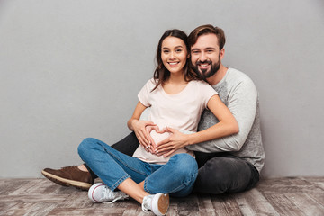 Smiling handsome man with his pregnant wife make heart gesture.