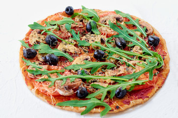 Fresh baked vegetarian pizza with mushrooms, tomatoes, rucola, black olives isolated on the white table. Close up view