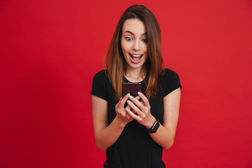 Photo of excited woman in black clothing typing text message or reading news on cell phone, over red background