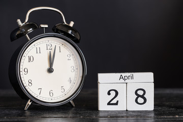 Wooden cube shape calendar for April 28 with black clock on black background