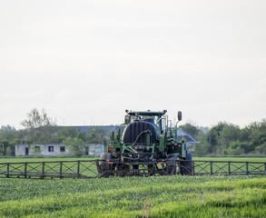 Tractor with a spray device for finely dispersed fertilizer. Tractor on the sunset background. Tractor with high wheels is making fertilizer on young wheat. The use of finely dispersed spray chemicals