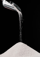 Fototapeta na wymiar sugar falling from metal scoop on pile isolated on black