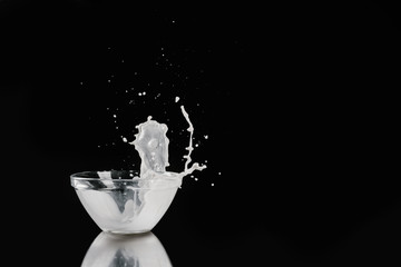 milk pouring out from bowl on black reflecting tabletop