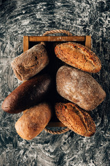 top view of arranged loafs of bread in wooden box on dark tabletop with flour