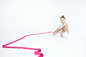 Rhythmic gymnastics caucasian blonde girl in dress for show performing athlete exercises with pink ribbon handling abilities showing flexibility and acrobat balance on white background isolated
