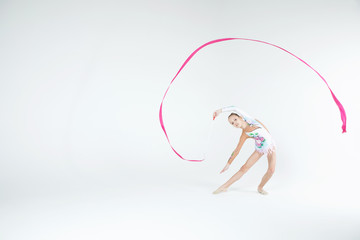 Rhythmic gymnastics caucasian blonde girl in dress for show performing athlete exercises with pink ribbon handling abilities showing flexibility and acrobat balance on white background isolated