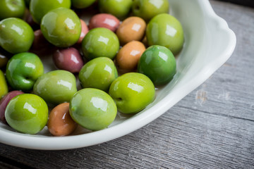 Fresh olives in white plate on the rustic background. Selective focus.