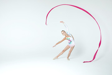 Rhythmic gymnastics caucasian blonde girl in dress for show performing athlete exercises with pink ribbon handling abilities showing flexibility and acrobat balance on white background isolated