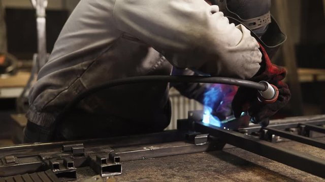 Master is bonding steel structure by welding. He is wearing protective mask and gloves and holding welding device