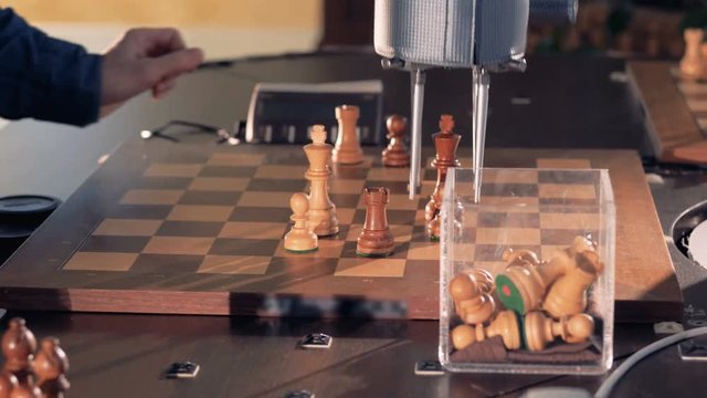 Robot playing chess with a man. Hand manipulator moves the chess and presses the key of the control watch. 4K.