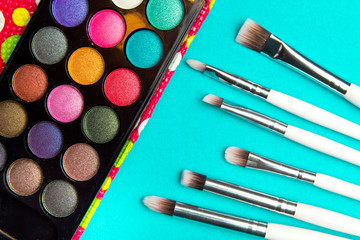 Obraz na płótnie Canvas Brushes with an eyeshadow palette in turquoise background. Decorative cosmetics for professional makeup. Eyeshadow colors trend.