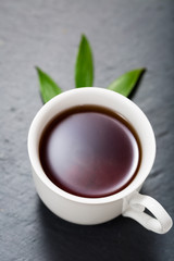 Detox tea concept, white cup on dark grey chalk board with green leaves, herbal tea  natural coffee, hot organic healthy purifying drink,  copy space for text, top view 