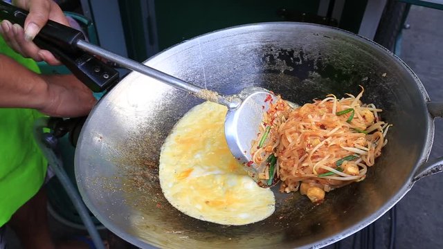 Street food : thai man is cooking pad thai noodle with egg at night food market in island Koh Phangan, Thailand