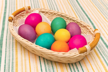 Colorful painted Easter eggs in a wicker basket on a striped tablecloth.
