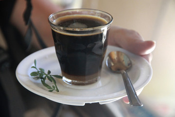 kawa po etiopsku podana w małym szklanym naczyniu na białym porcelanowym spodku - obrazy, fototapety, plakaty