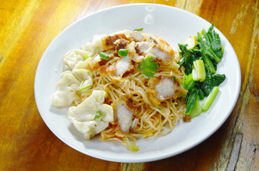 dry Chinese egg noodles topping crispy pork and dumpling on plate