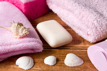Obraz na płótnie Canvas Pink sponges,a towel, soap, shampoo, body cream on wooden background with seashells .Cleansing spa accessories