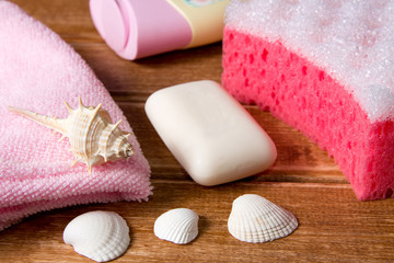 Obraz na płótnie Canvas Pink sponges for shower ,a towel, soap, shampoo, body cream on wooden background with seashells .Cleansing spa accessories