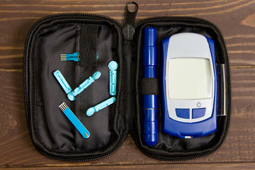 Glucometer with lancet pen and test strip lies in case bag on the wooden background. Diabetes