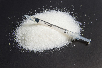 Insulin syringe and lots of sugar on black background. The concept of diabetes