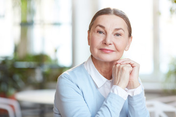 Happy mature woman with natural makeup looking at camera while spending time in cafe