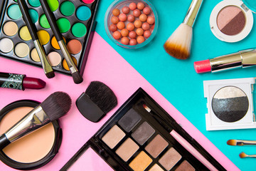 Brushes with an eyeshadow palette and lipstick in pink and mint geometric background. Decorative...