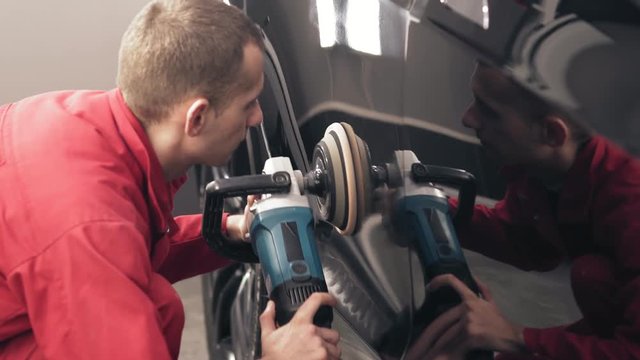 Polishing black car with a professional mashine. Worker of autocenter in red worksuit is cleaning every millimeter of new Tesla car side door.