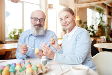 Contemporary aged couple preparing painted eggs for Easter before the holiday