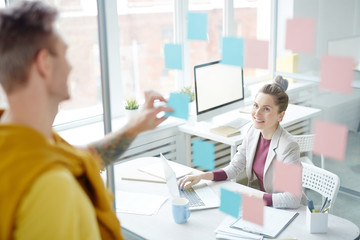 Young office manager looking at colleague through transparent wall while networking