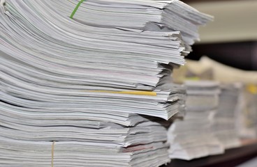 Stacks of paperwork sitting on an office desk in a messy but organized fashion. Suggests a stressful environment where deadlines must be met.