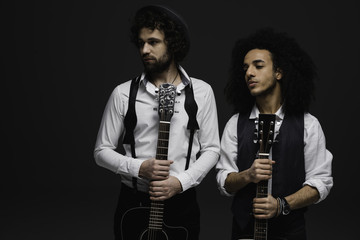 Obraz premium duet of handsome young musicians with acoustic guitars looking away on black
