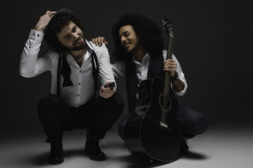 duet of happy musicians with guitar and harmonica sitting squat