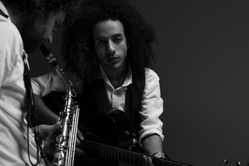 black and white shot of duet of musicians playing sax and acoustic guitar on black