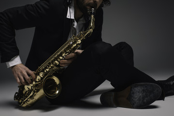 Naklejka premium cropped shot of musician playing saxophone while sitting on floor