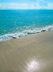 Sandy beach and sea water in summer sunny day.
Beautiful ocean view with a small smooth waves and reflection of sunshine on sand. Miami, FL, USA. Travel vacation concept.