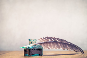 Quill ink pen with inkwell on wooden desk front concrete wall background. Vintage old style...