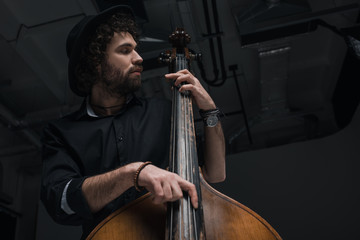bottom view of young handsome musician playing contrabass - obrazy, fototapety, plakaty