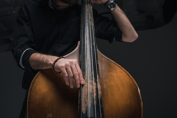 cropped shot of man playing contrabass on black - obrazy, fototapety, plakaty