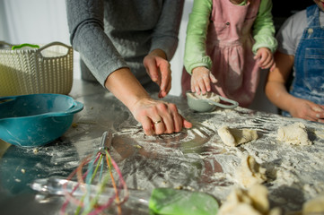 Mom teaches two little daughters to cook from dough.